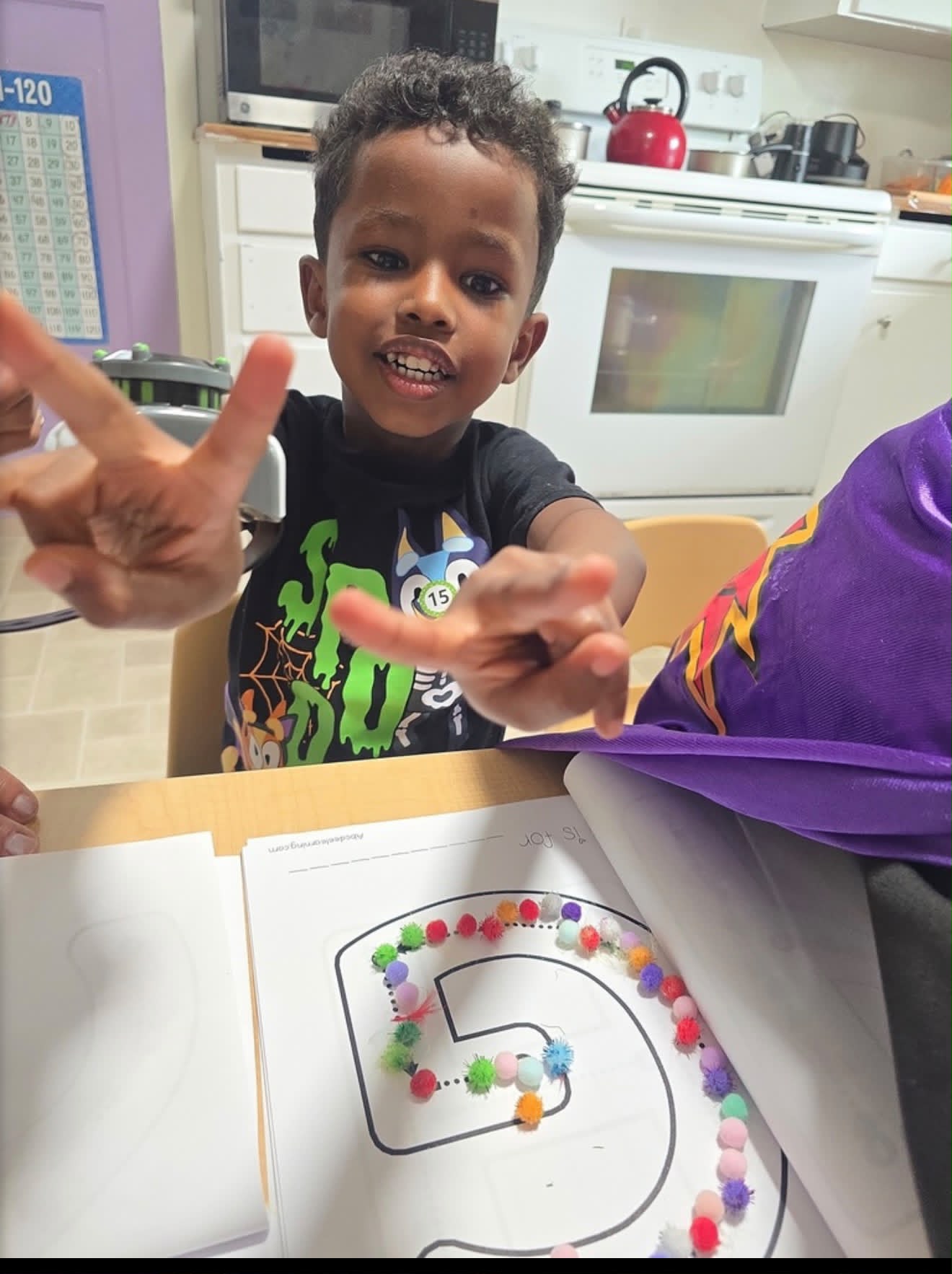 Preschooler counting with colorful pom-poms on a number tracing sheet