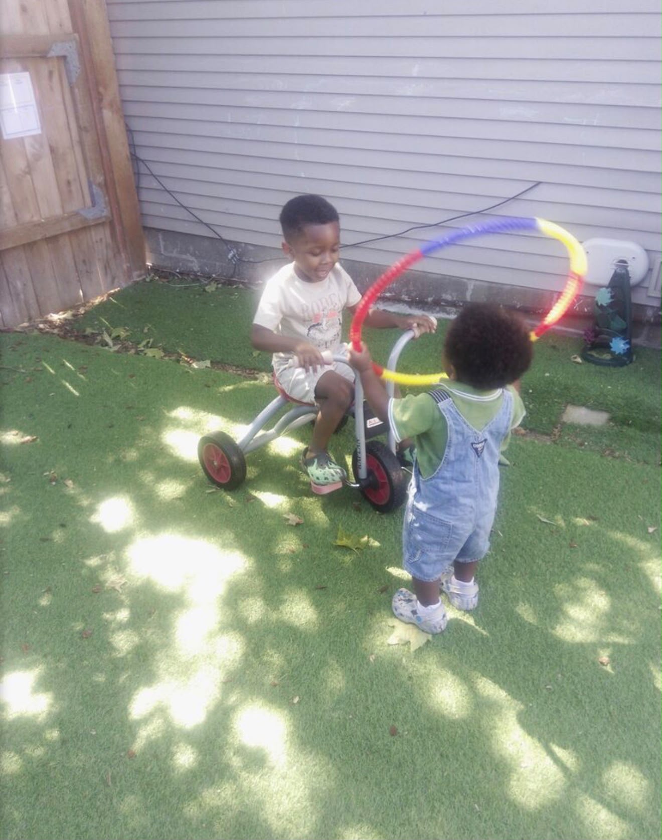 Two friends playing with a hoop and tricycle outside